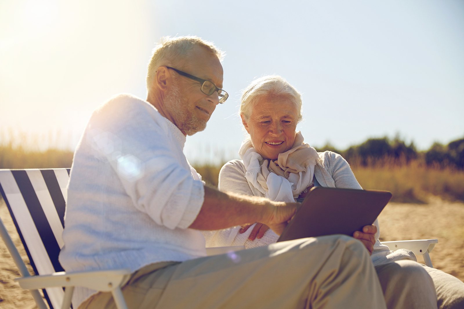 Elderly couple using m.Care tablet while on vacation at the beach