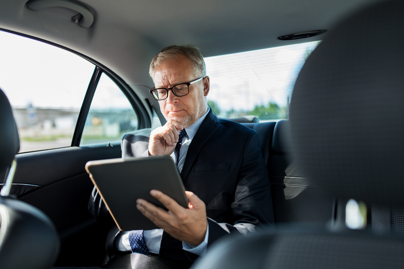 Businessman using m.Care tablet while traveling in back seat of car