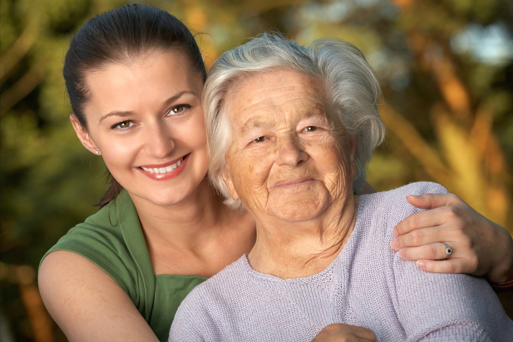 Young female caregiver hands hugging old woman